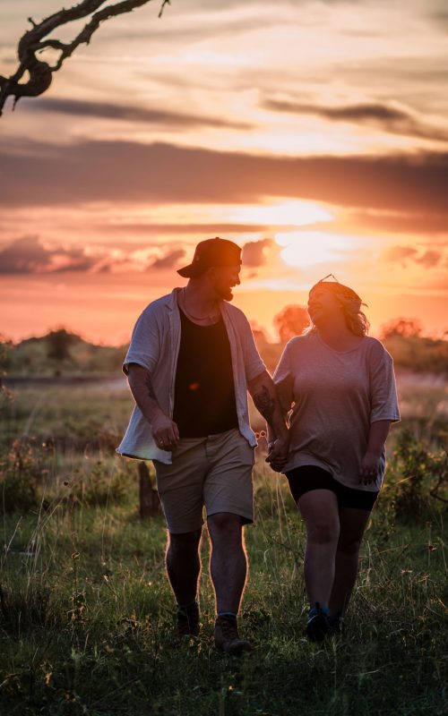 Brautpaar läuft Hand in Hand über die offene Savanne. Die untergehende Sonne taucht die Landschaft in goldenes Licht.